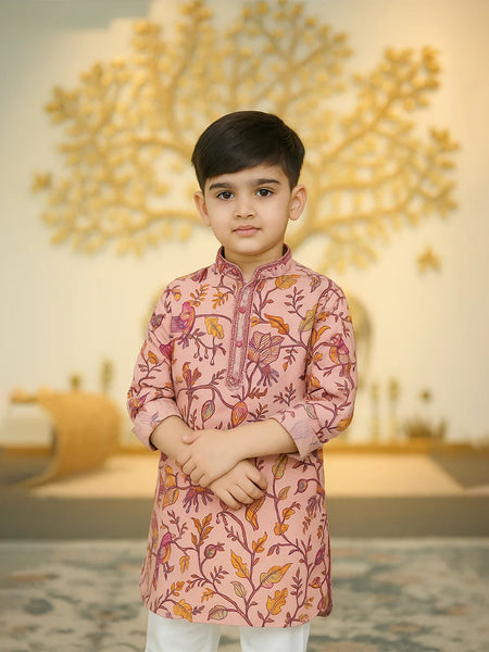 Young boy wearing a pink traditional outfit with floral patterns in a decorated indoor setting.
