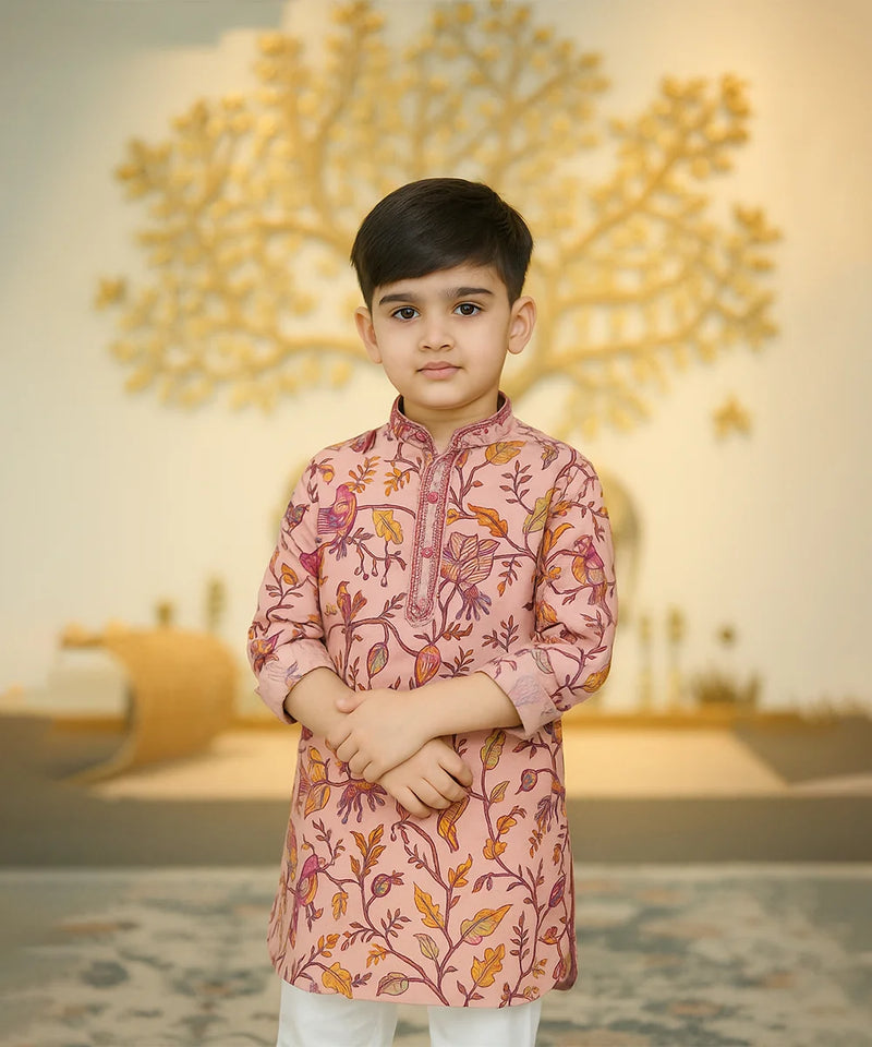 Young boy wearing a pink traditional outfit with floral patterns in a decorated indoor setting.