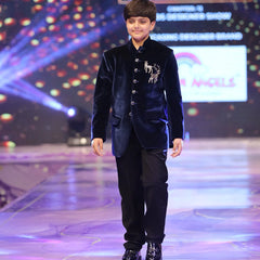 Young boy in a formal outfit walking on a stage with colorful lights and branding in the background.