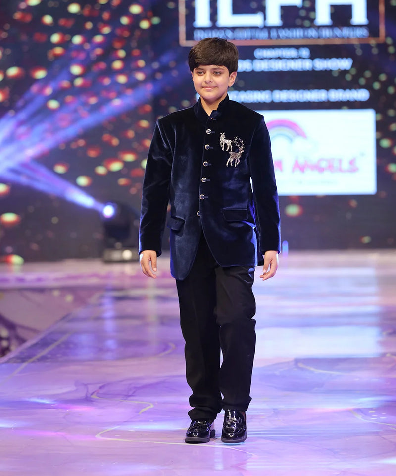 Young boy in a formal outfit walking on a stage with colorful lights and branding in the background.