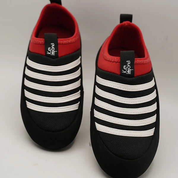 Kids' black slip-on sneakers with bold white stripes and red collar, Jaipur