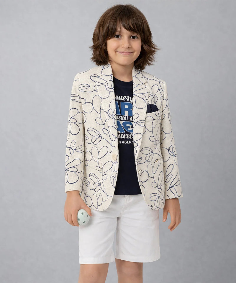 Child wearing a patterned blazer and white shorts on a plain background