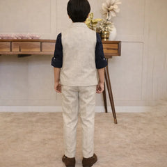 Child wearing a formal outfit standing in a room with a wooden desk and decorative items.
