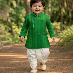 Child wearing a green kurta with white dhoti standing outdoors on a path.