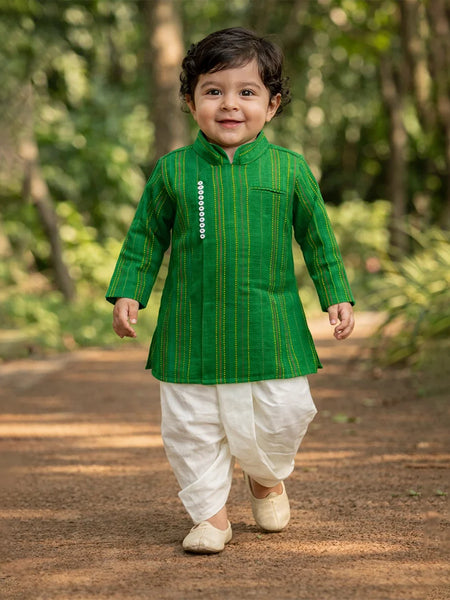 Child wearing a green kurta with white dhoti standing outdoors on a path.