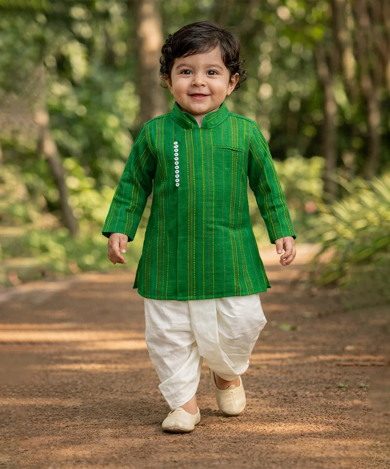 Child wearing a green kurta with white dhoti standing outdoors on a path.