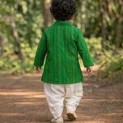Child wearing a green traditional outfit walking on a dirt path with greenery in the background