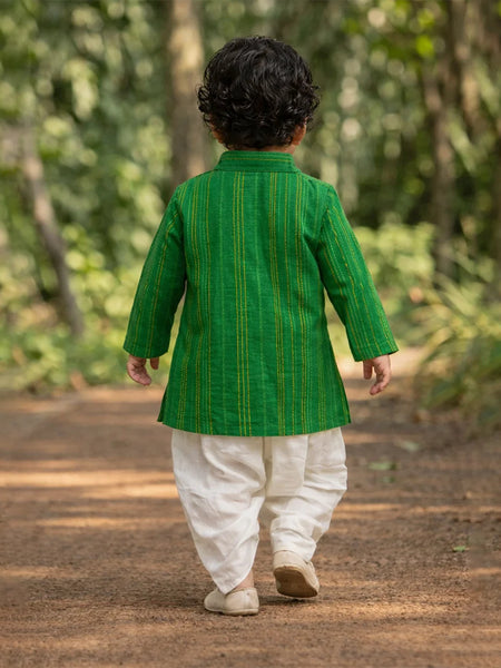 Child wearing a green traditional outfit walking on a dirt path with greenery in the background