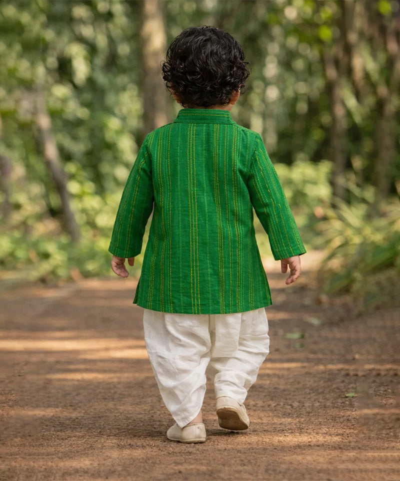 Child wearing a green traditional outfit walking on a dirt path with greenery in the background