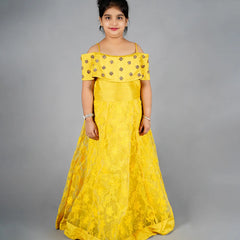 Young girl wearing a yellow off-shoulder dress with floral embellishments on a gray background