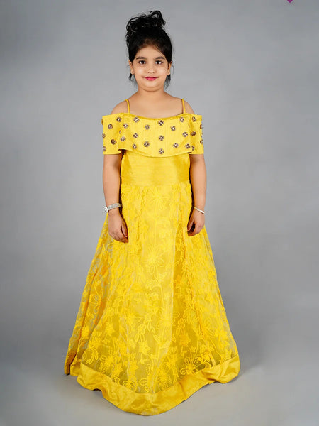 Young girl wearing a yellow off-shoulder dress with floral embellishments on a gray background