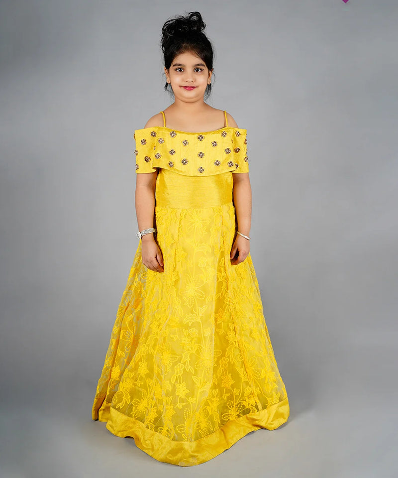 Young girl wearing a yellow off-shoulder dress with floral embellishments on a gray background