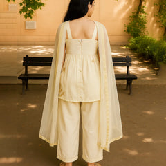 Woman in a cream-colored outfit standing outdoors with a bench and trees in the background