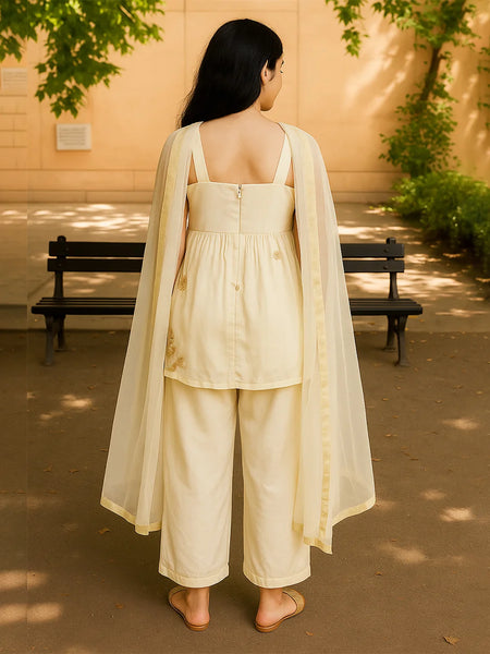 Woman in a cream-colored outfit standing outdoors with a bench and trees in the background