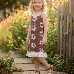 Young girl in a brown dress with white floral patterns standing in a garden.