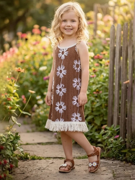 Young girl in a brown dress with white floral patterns standing in a garden.