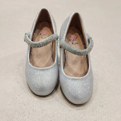 Pair of silver glitter shoes with embellished straps on a beige background