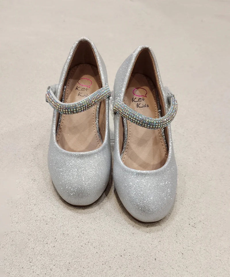 Pair of silver glitter shoes with embellished straps on a beige background