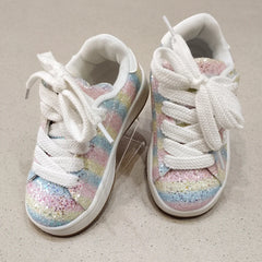 Pair of white sneakers with colorful glittery soles on a beige surface