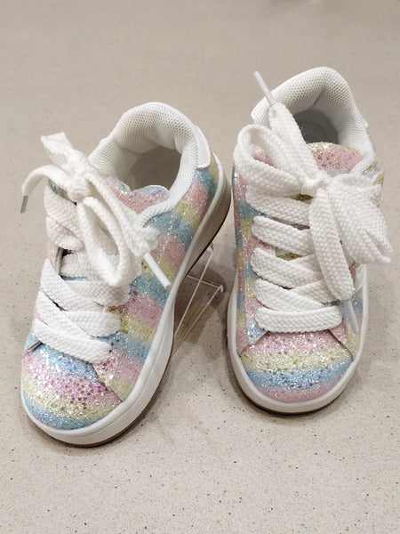 Pair of white sneakers with colorful glittery soles on a beige surface