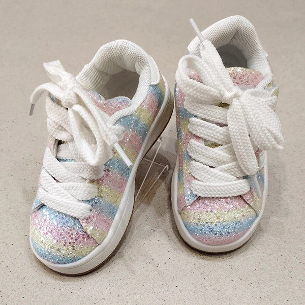 Pair of white sneakers with colorful glittery soles on a beige surface