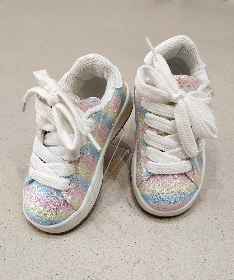 Pair of white sneakers with colorful glittery soles on a beige surface