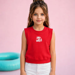 A young girl with her hair in a high bun stands against a solid pink background, wearing a bright red sleeveless crop top sweatshirt with a white graphic that reads 'Moms Just Want Off' and white pants.