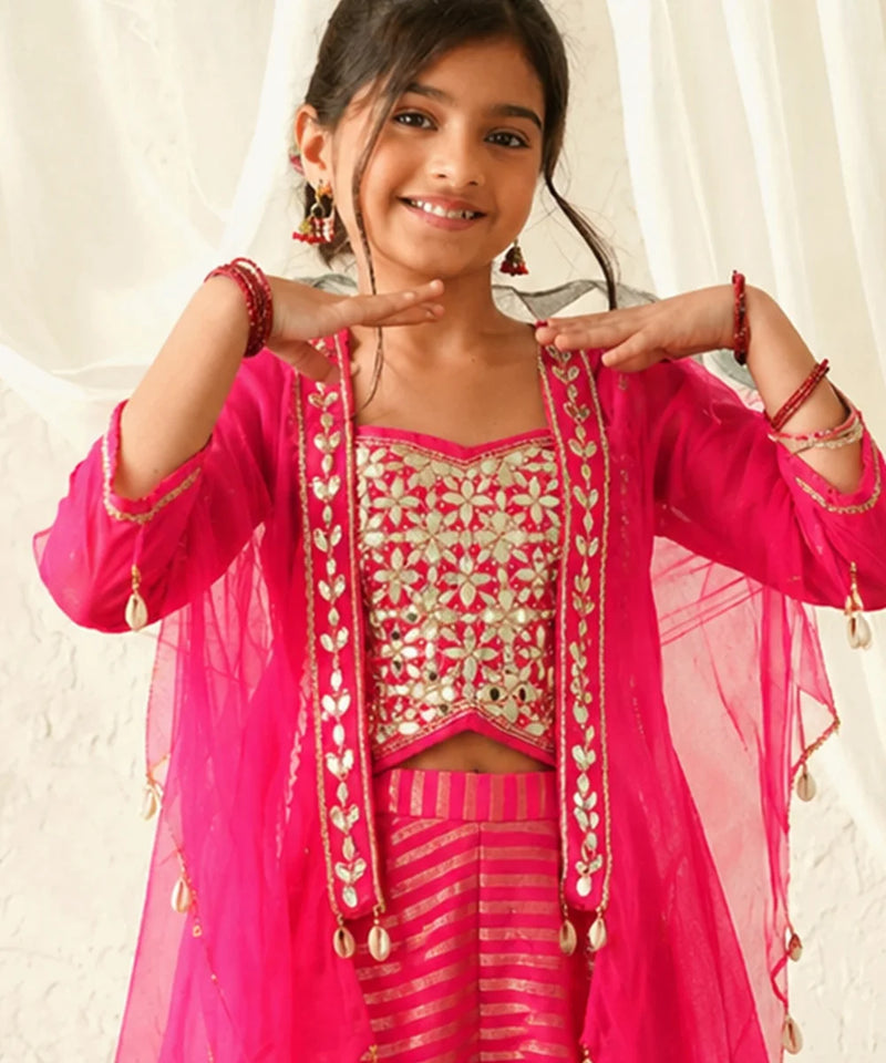 Young girl in a pink traditional outfit with gold embroidery against a white curtain background