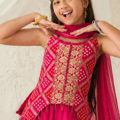 Young girl wearing a pink and gold traditional outfit with a scarf, smiling against a light background.