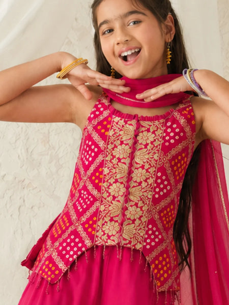 Young girl wearing a pink and gold traditional outfit with a scarf, smiling against a light background.