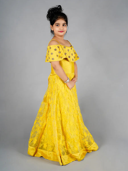 Young girl wearing a yellow off-shoulder dress with floral patterns on a gray background