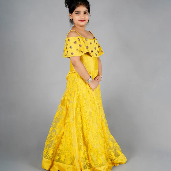 Young girl wearing a yellow off-shoulder dress with floral patterns on a gray background