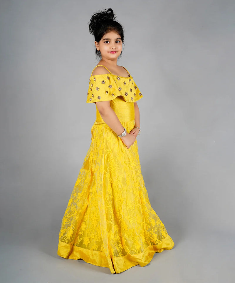 Young girl wearing a yellow off-shoulder dress with floral patterns on a gray background