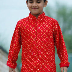 Child wearing a red traditional outfit with gold patterns outdoors.