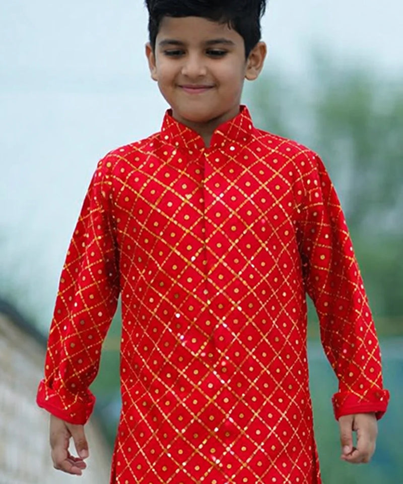 Child wearing a red traditional outfit with gold patterns outdoors.