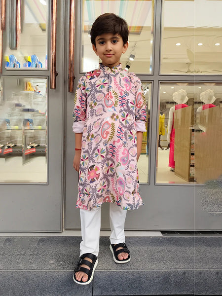 Child wearing a floral kurta with white pants standing in front of a store entrance.