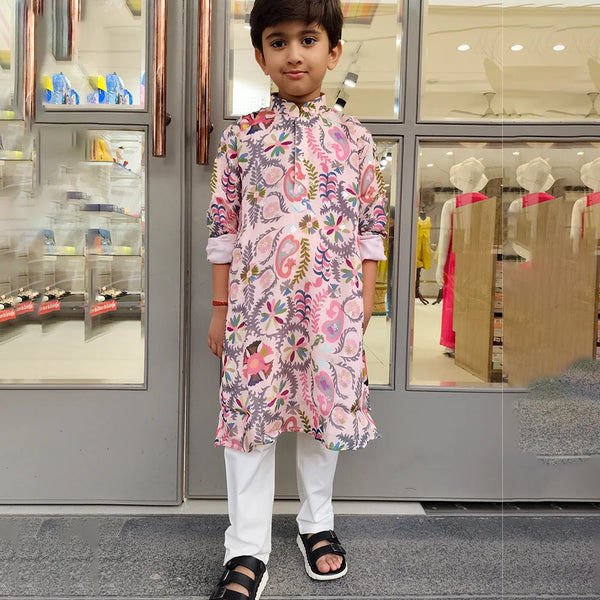 Child wearing a floral kurta with white pants standing in front of a store entrance.