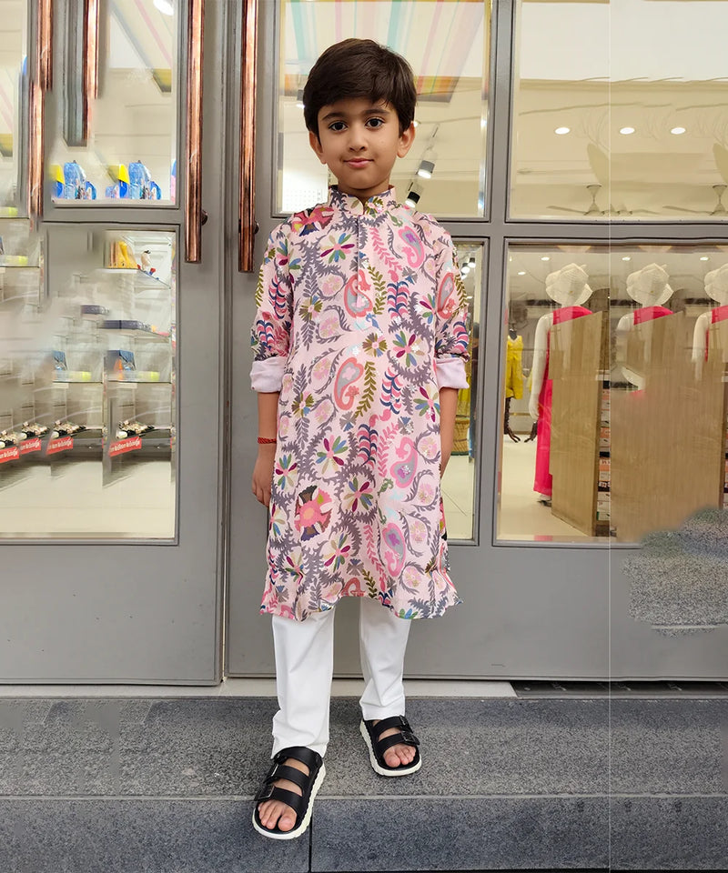 Child wearing a floral kurta with white pants standing in front of a store entrance.