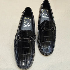 Black crocodile-patterned loafers with a brand logo on a beige background