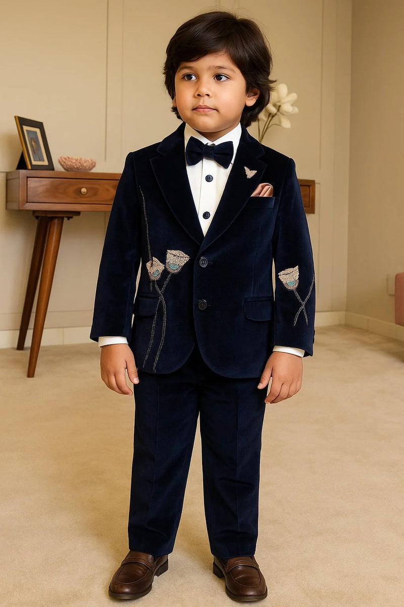Young boy in a formal navy suit with bow tie standing indoors.
