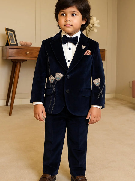 Young boy in a formal navy suit with bow tie standing indoors.