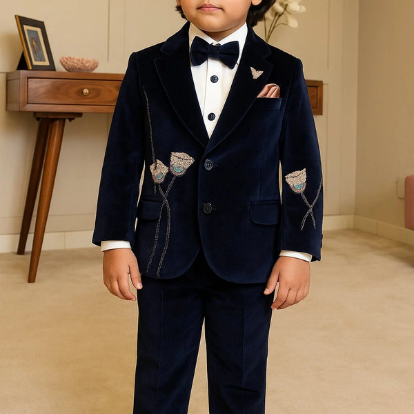 Young boy in a formal navy suit with bow tie standing indoors.