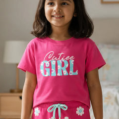 Young girl wearing a pink 'Cutiee Girl' shirt and matching pants in a room.