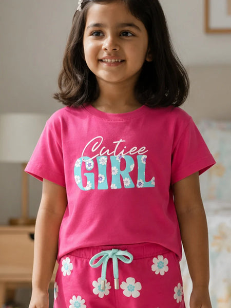 Young girl wearing a pink 'Cutiee Girl' shirt and matching pants in a room.