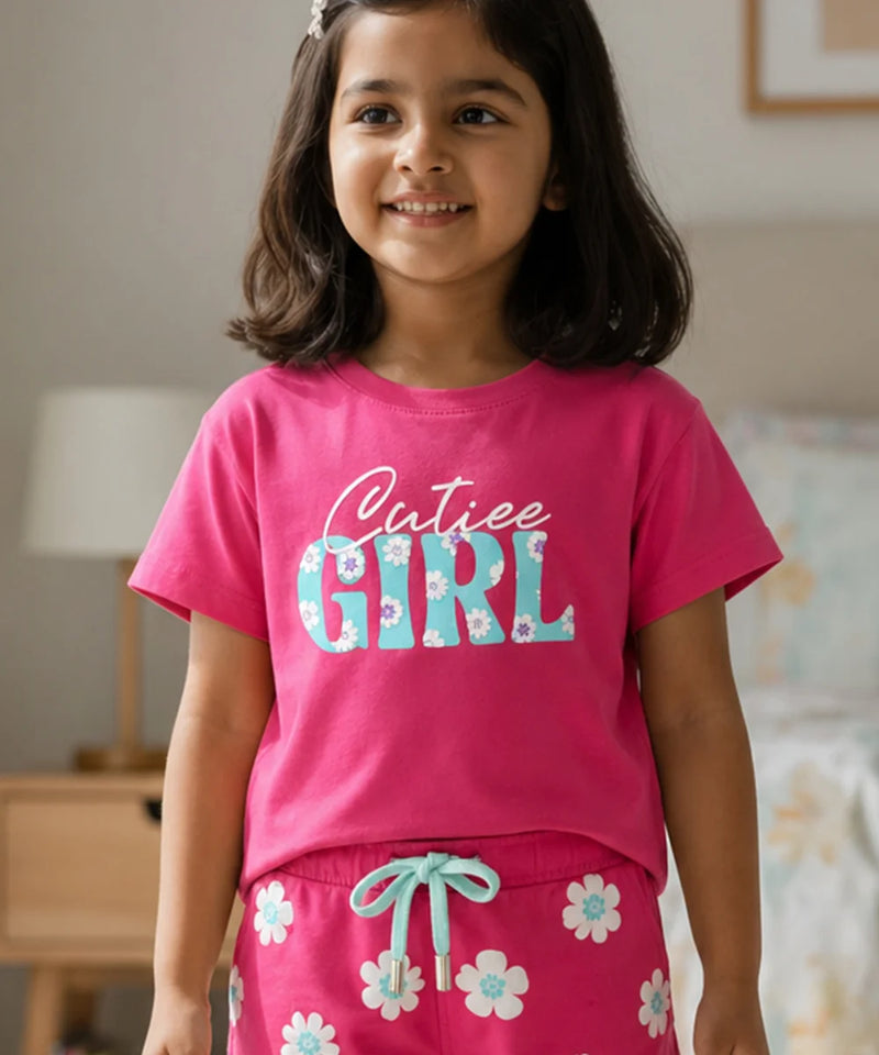 Young girl wearing a pink 'Cutiee Girl' shirt and matching pants in a room.