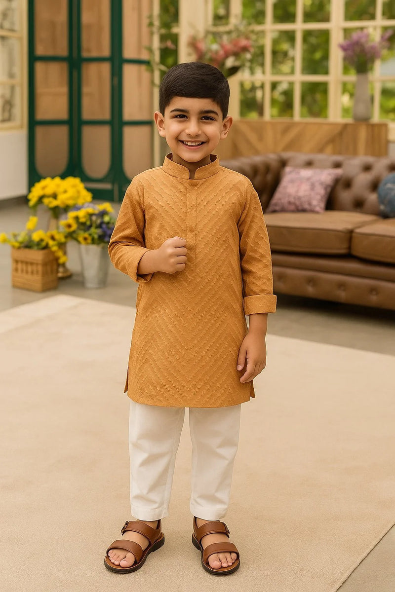Young boy in a mustard kurta with white pants standing in a living room.