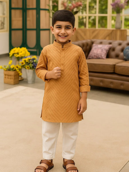 Young boy in a mustard kurta with white pants standing in a living room.