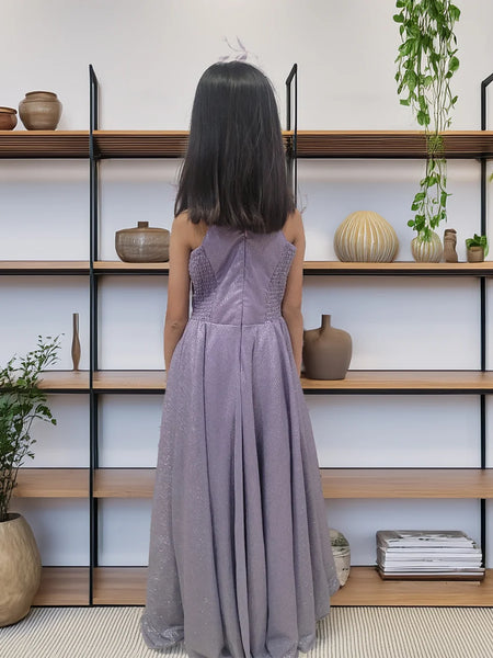 Girl in a long purple dress standing in front of a bookshelf with decorative items.