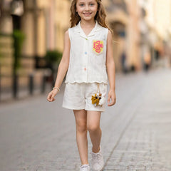 Young girl in a white outfit with floral details walking on a street.