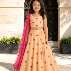 Young girl in a peach dress with red heart patterns and a pink dupatta standing in front of an archway.